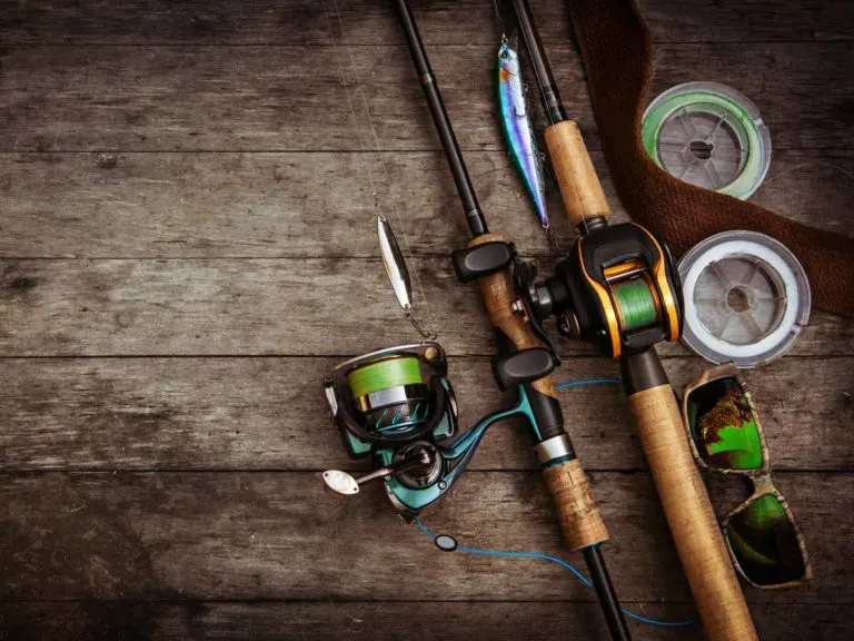 Angler holding multiple fishing rods comparing different types by a lake at sunrise