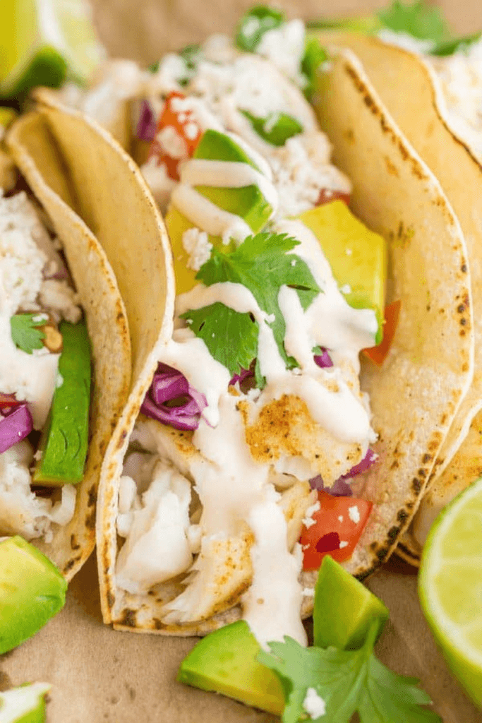 Homemade fish tacos with tilapia, creamy white sauce, and lime wedges on plate