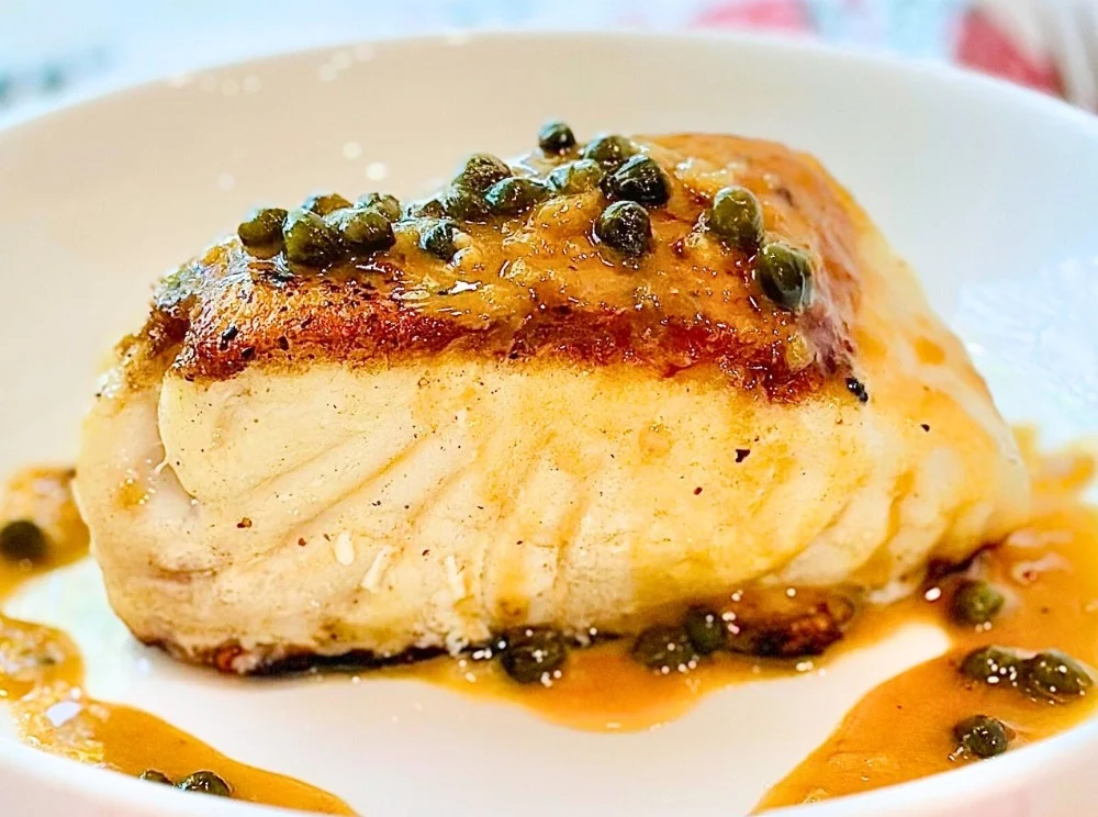 Pan-seared sea bass with crispy golden skin and lemon beurre blanc sauce on white plate